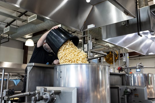 Worker pours bucket of popcorn into vat