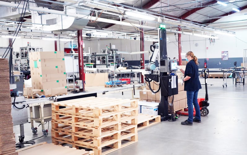 Mujeres trabajando junto a un robot paletizador en una fábrica.