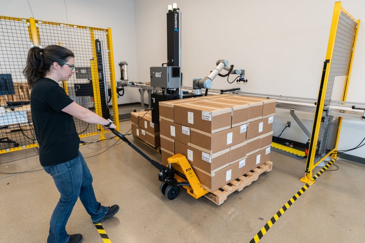 Worker bringing a pallet near a palletizing robot.