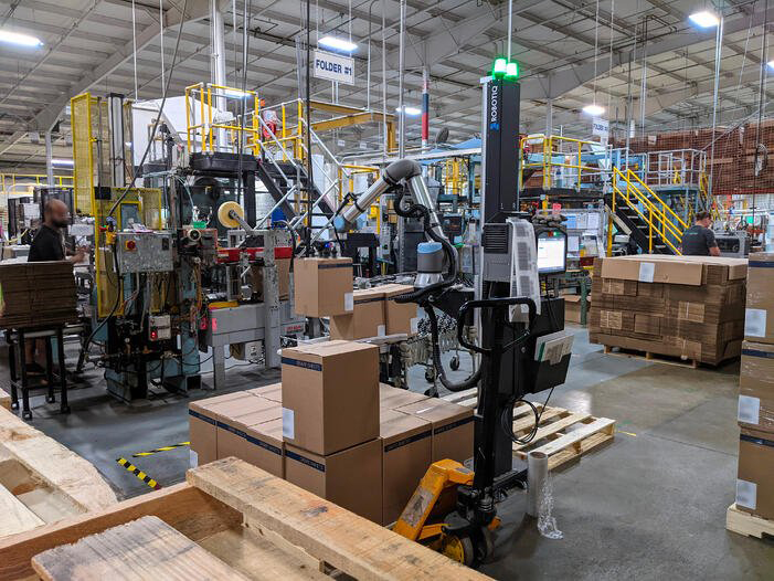 Collaborative robot being used to palletize cardboard boxes in a manufacture.